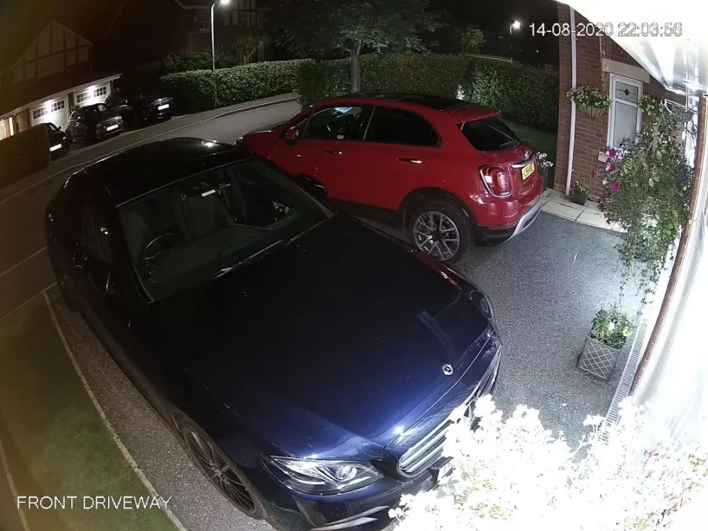 Night CCTV view of a front driveway showing a dark blue Mercedes in the foreground and a red compact SUV by the house, timestamp 14-08-2020 22:03:56